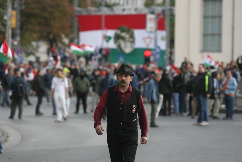 Protester walking toward the camera with a giant lyukas zászló (hole-flag) banner in the background